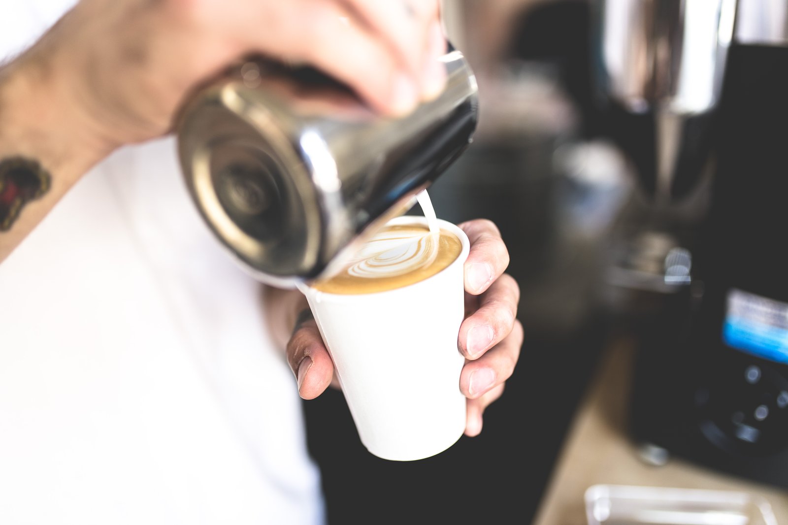 A barista pouring steamed milk into a coffee cup