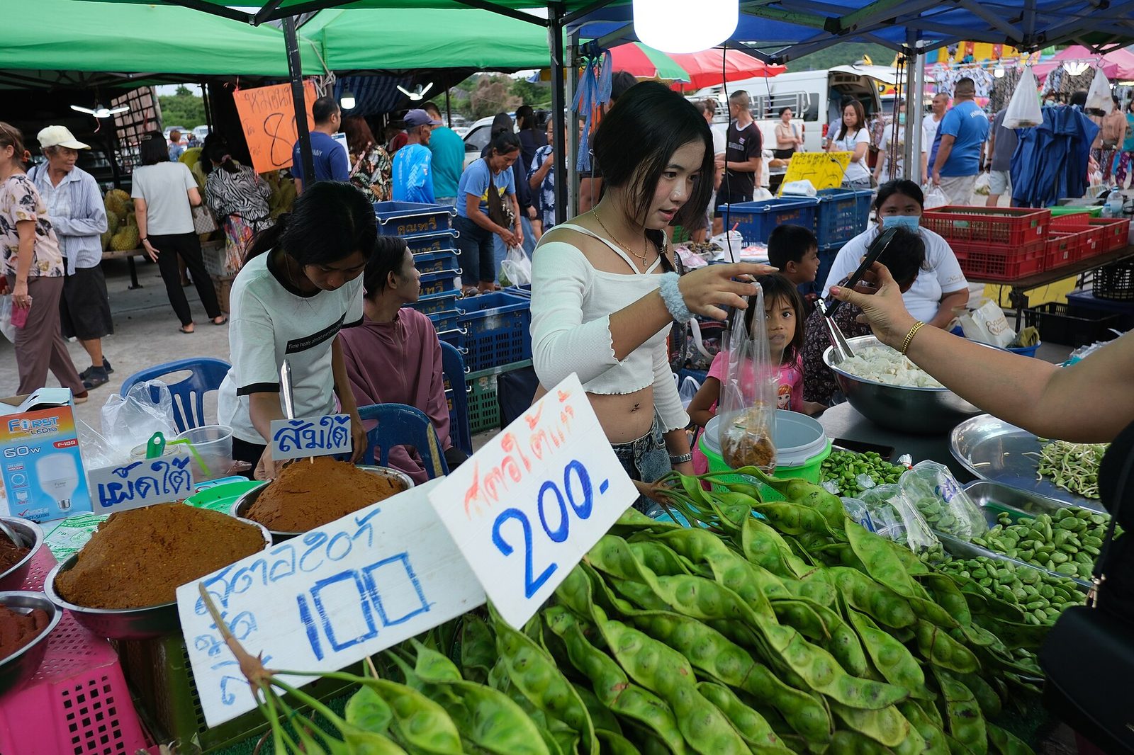 Shoppers browsing a bustling outdoor market with vendors selling fresh produce under colorful canopies